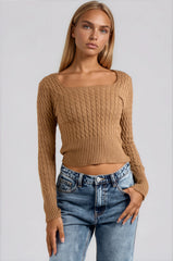 Woman wearing a brown ribbed sweater and blue jeans on a light gray background